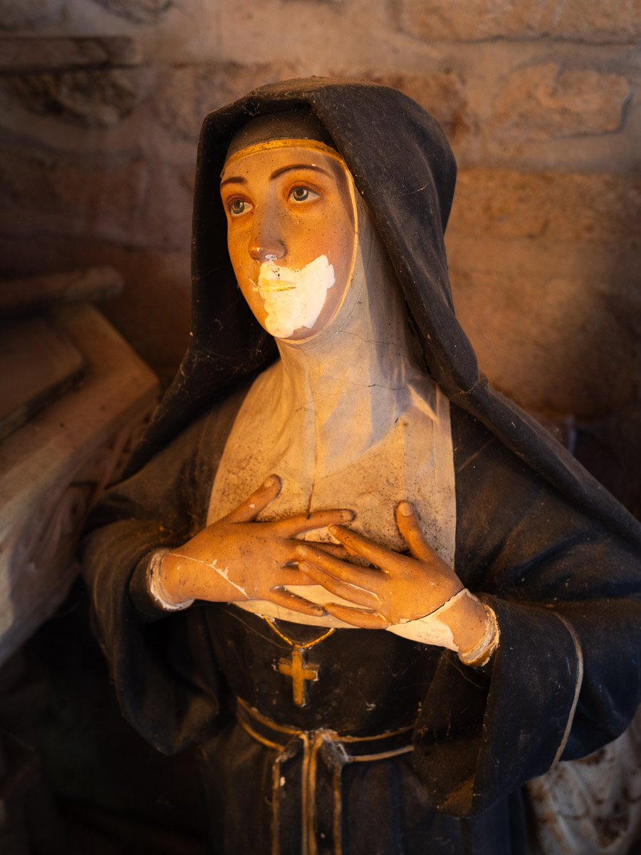 Une statue d'une mystique regardant le ciel avec ferveur, réparée au niveau. Le plâtre a été réparé sur ses mains et sa bouche mais la peinture n'est pas refaite.