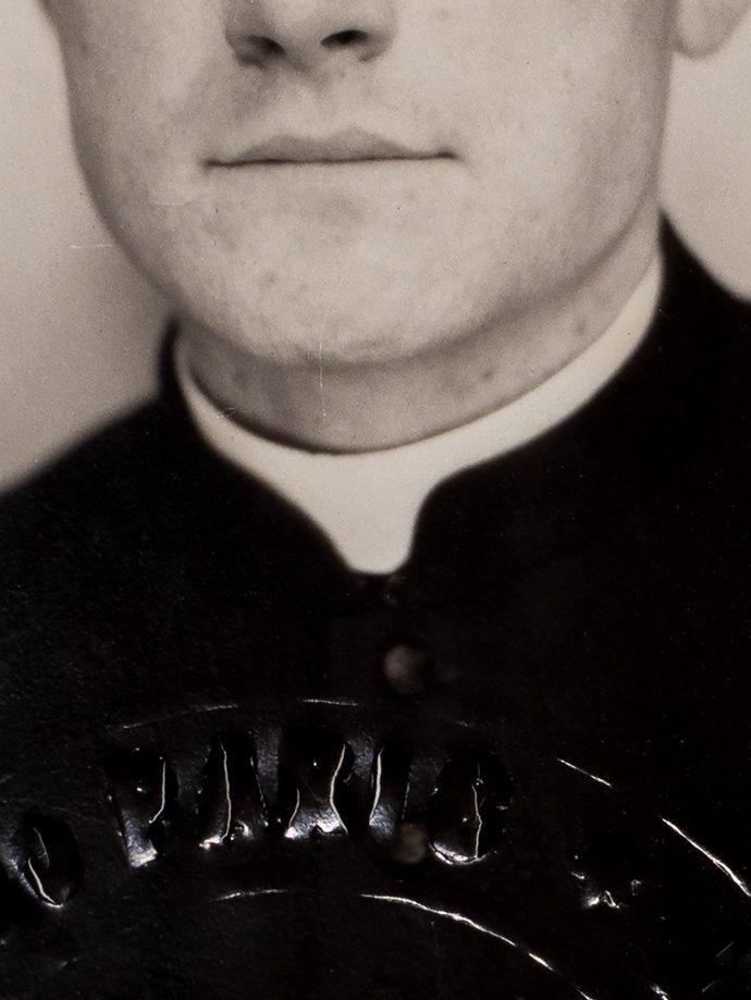 Détail d'une photographie d'identité, coupée au niveau des yeux et centrée sur le col romain de l'homme photographiée.